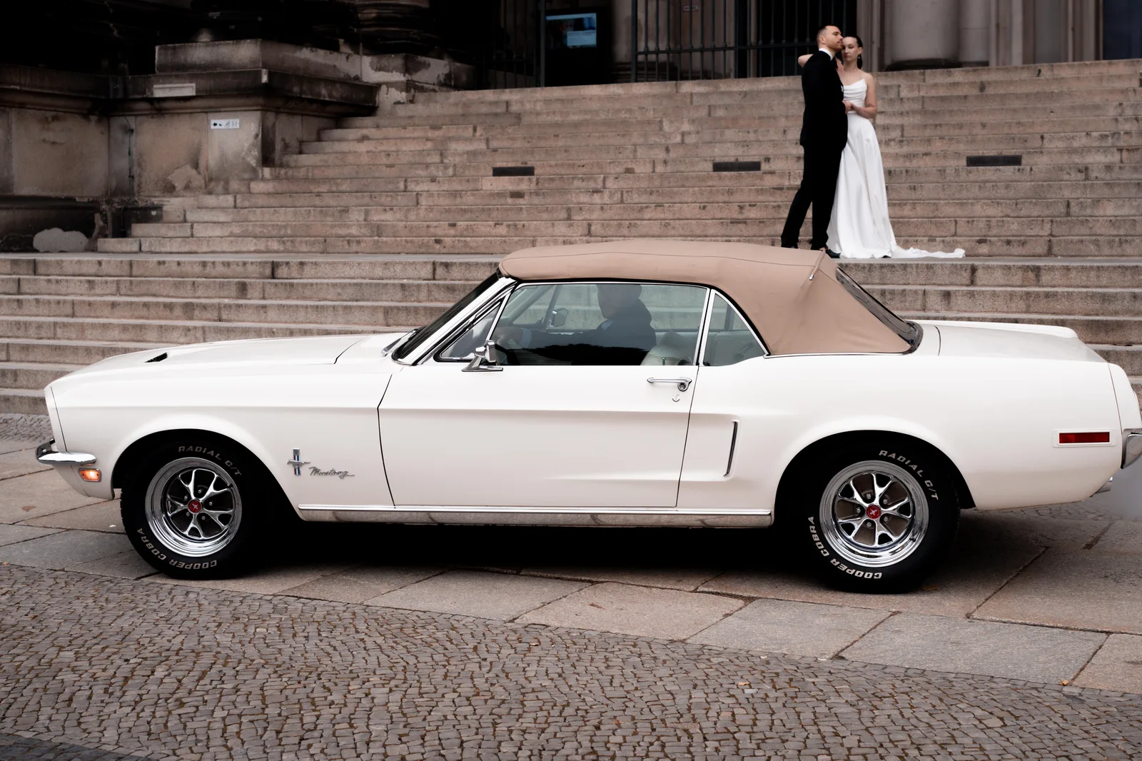 Brautpaar mit dem weißen Mustang an einer Treppe